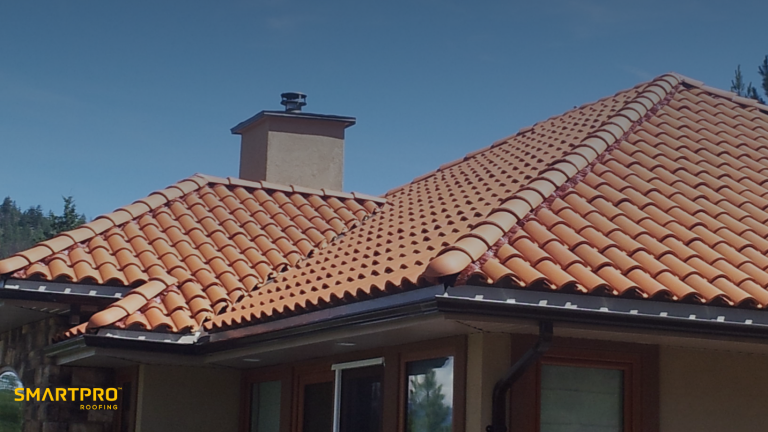 House with a clay tile roof under a clear blue sky, featuring red clay tiles and a chimney. SmartPRO Roofing logo displayed at the bottom.