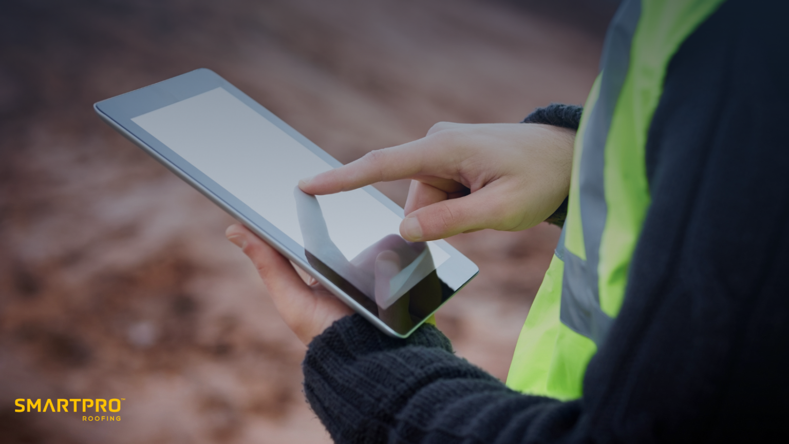 A person wearing a safety vest is holding a tablet computer, focused on their task in a professional environment.