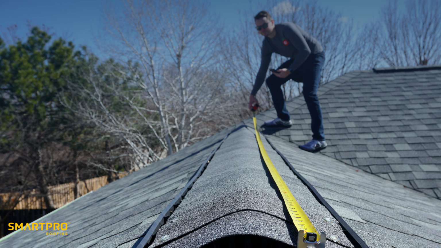 Roofing professional measuring the roof ridge with a yellow tape measure for SmartPRO Roofing.