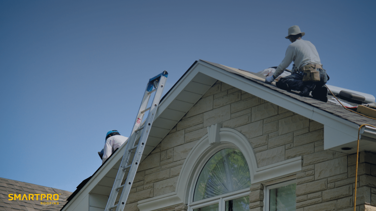 Two men collaborating on the roof of a house, engaged in construction work under clear skies.