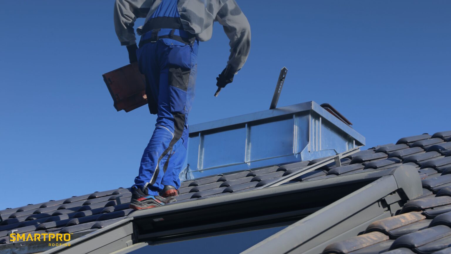 A man stands on a roof beside a ladder, holding a tool, preparing for maintenance or repair work.