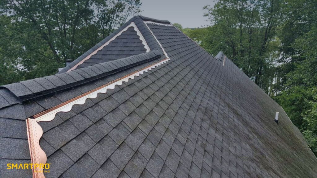 A close-up of a roof featuring dark shingles and shiny copper flashing along the edges.