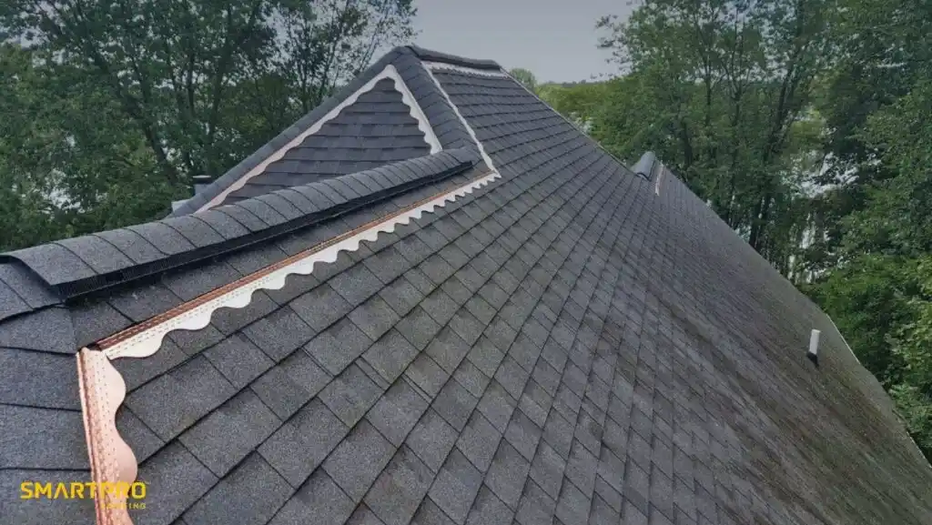 A close-up of a roof featuring dark shingles and shiny copper flashing along the edges.