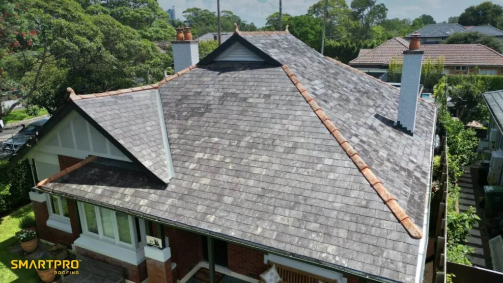 A house roof featuring grey shingles and a prominent chimney against a clear sky.