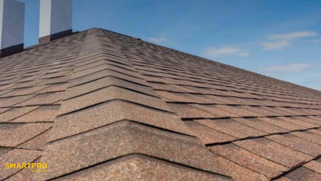 Close-up of a shingled roof against a clear blue sky. The brown shingles form a neat pattern, conveying durability and protection. "SMARTPRO Roofing" logo is visible.