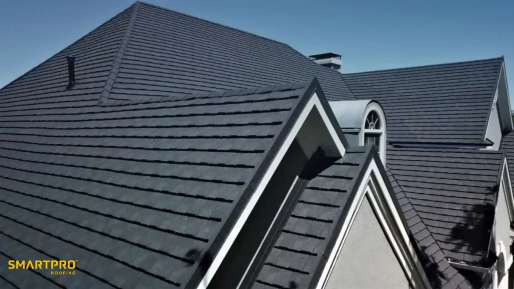 Image of a house with a modern, dark gray shingle roof under a clear blue sky. The roof features multiple gables and a chimney.