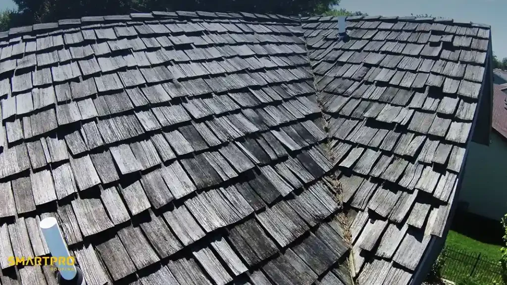 A weathered wooden shingle roof with a central valley, showing signs of aging and wear. Two white vents are visible, conveying a rustic atmosphere.