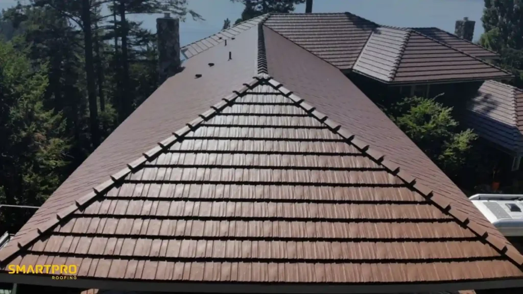 Aluminum Shingles: Benefits, Costs, Styles, and Installation Guide 10 Aerial view of a large, brown tiled roof with snow guards, surrounded by tall evergreen trees. The scene is bright and serene, suggesting a crisp day.