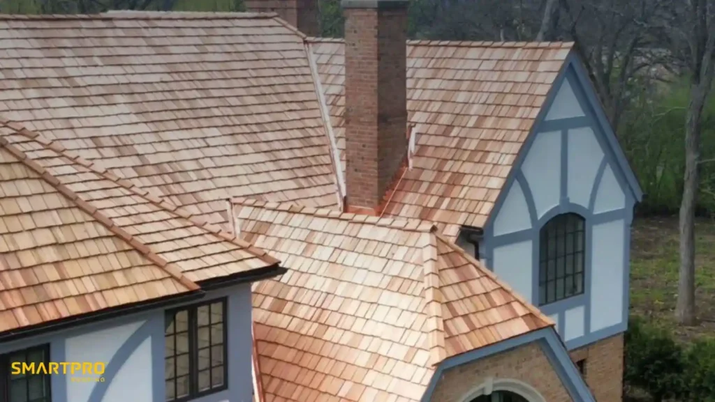 What Are Cedar Shingles? Smooth, Stylish Wood Roofing Explained 11 A Tudor-style house with light brown wooden shingles and two brick chimneys. The exterior features white and blue decorative trim, surrounded by trees.