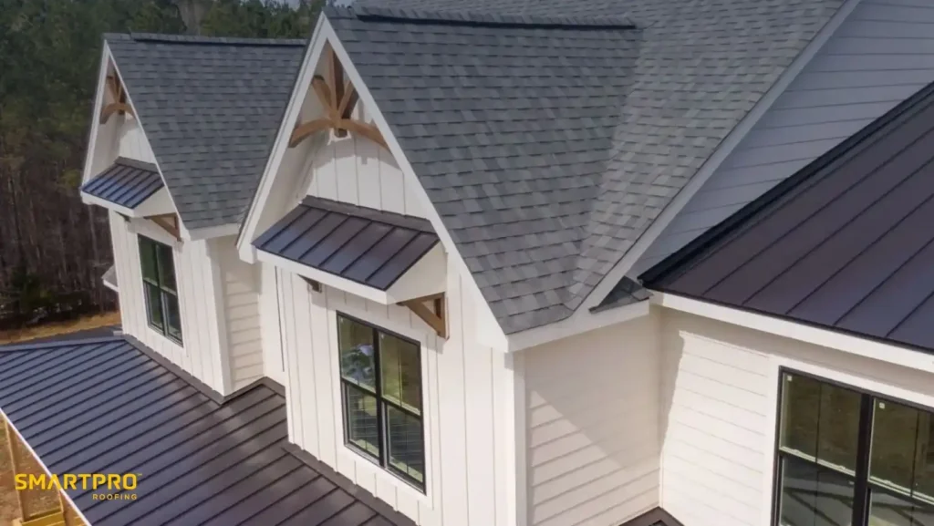 Are Metal Shingle Roofs Worth the Cost? Benefits & Lifespan 10 Aerial view of a house with light gray roofing shingles and white siding. Two dormer windows with metal awnings add a modern touch. Forest in background.