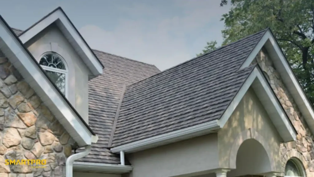Are Metal Shingle Roofs Worth the Cost? Benefits & Lifespan 12 Stone-faced house with a steeply pitched roof featuring gray shingles. An arched window is visible, with trees in the background, under a clear sky.