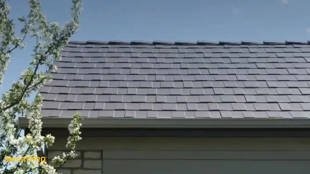 Steel Shingles: Durable, Stylish, and Long-Lasting Roofing Solutions 10 Solar roof tiles cover a house roof under a clear blue sky. A blossoming tree with white flowers is on the left, conveying a sense of spring.