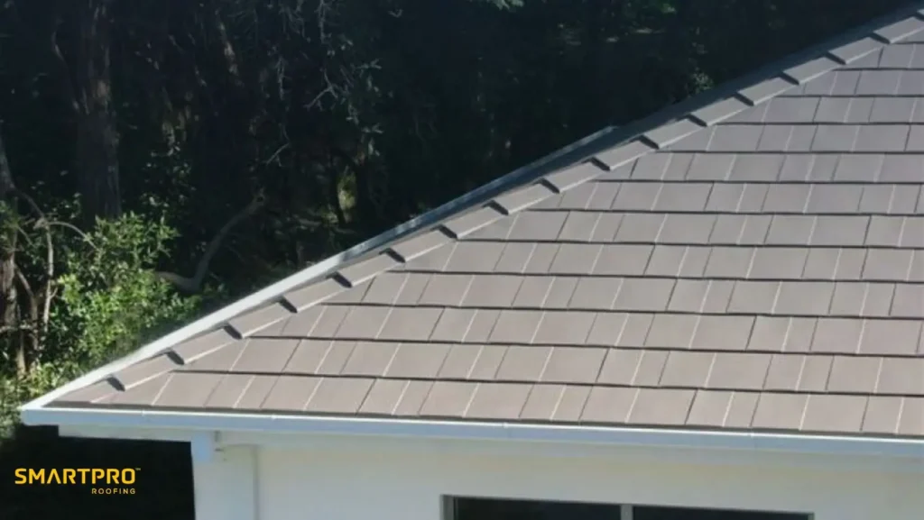 Aluminum Shingles: Benefits, Costs, Styles, and Installation Guide 11 Roof with gray shingles and neat rows on a white house, surrounded by trees. The "SMARTPRO ROOFING" logo is in the bottom left corner.
