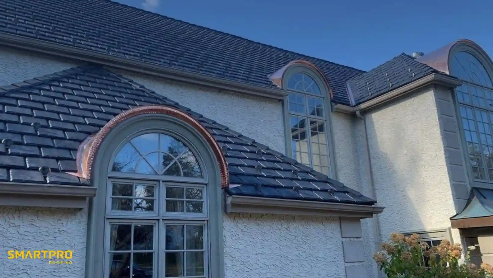 Elegant house exterior with textured beige walls, a slate roof, and arched windows. Autumn sunlight enhances the inviting and serene ambiance.