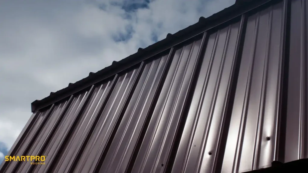 Metal Shingles vs. Standing Seam Metal Roofing 10 Close-up of a shiny metal roof against a cloudy sky, reflecting sunlight. The words "SMARTPRO ROOFING" are in the bottom left corner.