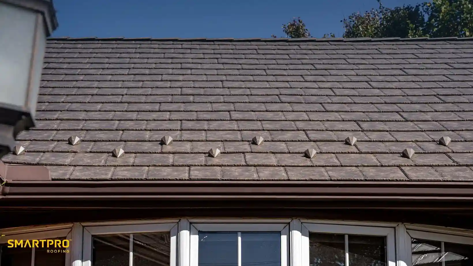 A neatly laid, brown shingle roof under bright blue sky, with subtle geometric shapes on the shingles. A source of natural light softens the scene.