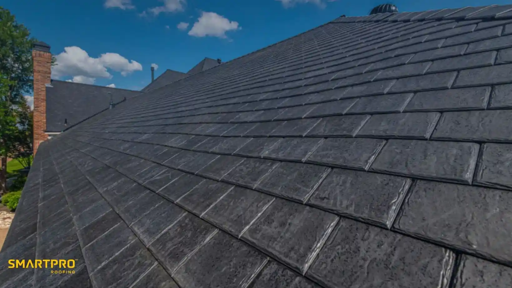 Close-up view of a gray shingle roof under a blue sky with scattered clouds. The roof tiles are neatly aligned, suggesting durability and quality craftsmanship.