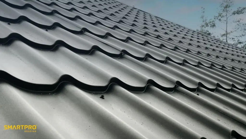 Metal Shingles vs. Standing Seam Metal Roofing 11 Close-up of a shiny, wavy metal roof under a clear blue sky. The scene conveys a sense of durability and modern design. Company logo in the corner.