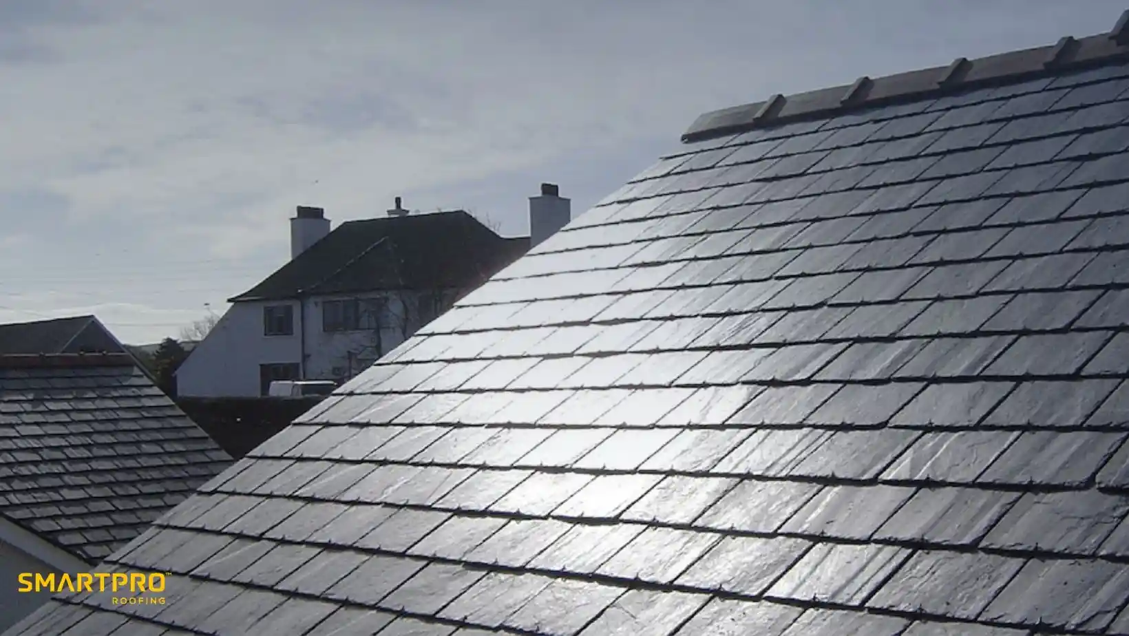 Shiny, slate-tiled roof reflecting sunlight against a partly cloudy sky. Nearby, suburban houses are visible. The scene conveys a calm, bright atmosphere.
