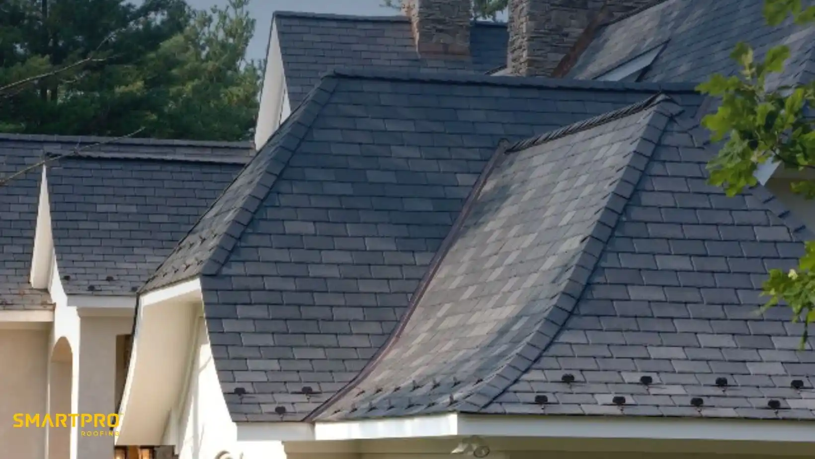 Slate roof shingles on a house with chimneys, against a backdrop of trees and sky. The scene conveys a serene, well-maintained architectural style.