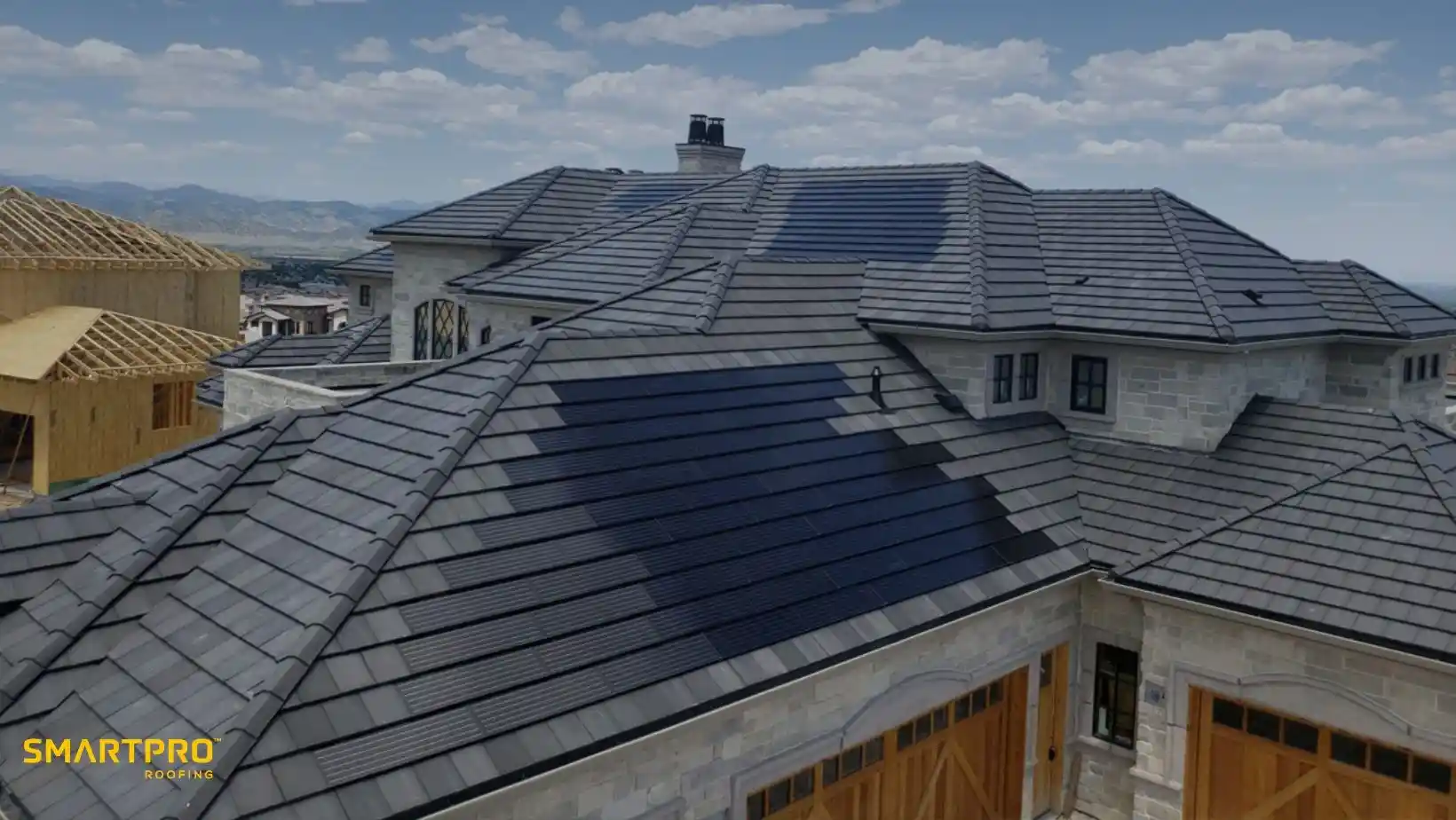 Rooftop of a stone house with sleek, dark-colored tiles under a blue sky. A building under construction is visible nearby. Calm and modern ambiance.