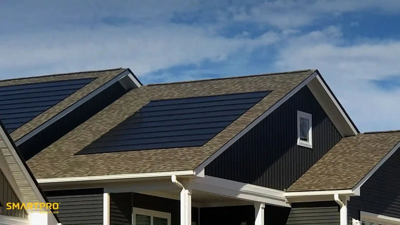 A modern house with dark blue siding features a roof outfitted with solar panels. The sky is clear and blue, suggesting a sunny day.
