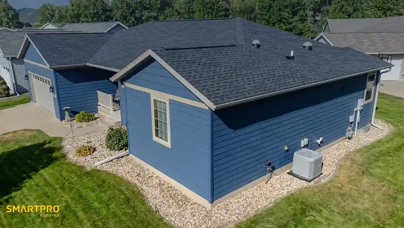 Fiber Cement Shingles: A Durable Alternative to Wood 10 A blue house with a dark roof and beige trims, surrounded by a neat lawn and a gravel path. An air conditioning unit is on the side. Sunny day, suburban setting.
